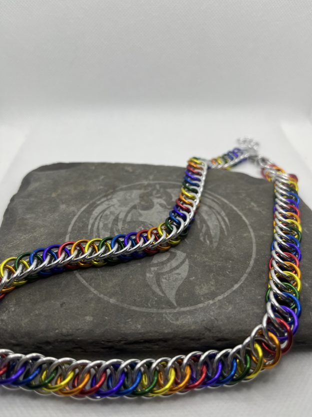 A chainmaille chain completed in the Persian 4 in 1 weave. It has alternating rings in the colors of the traditional pride flag--red, orange, yellow, green, blue, and purple. Silver rings are intermixed forming a bright backdrop to the alternating rings.