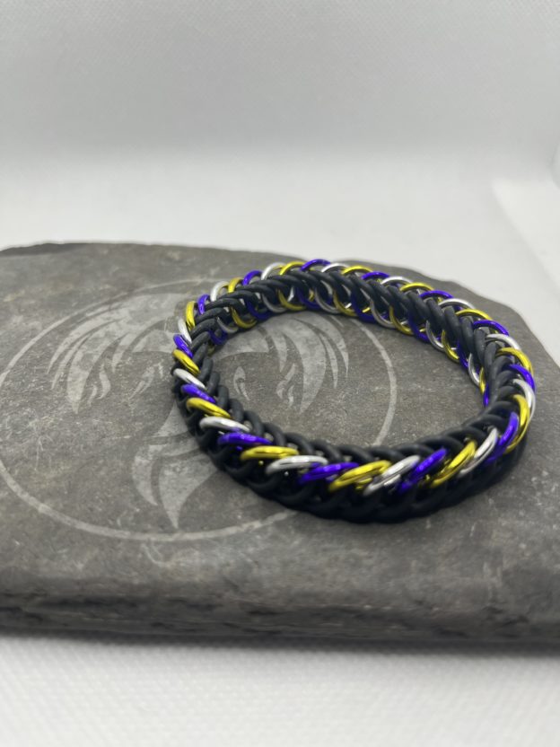 A chainmaille bracelet made with the persian 4 in 1 weave. This bracelet represents the Non-Binary Pride flag. It is made of black EPDM rings, and purple, silver, and yellow anodized aluminium rings.