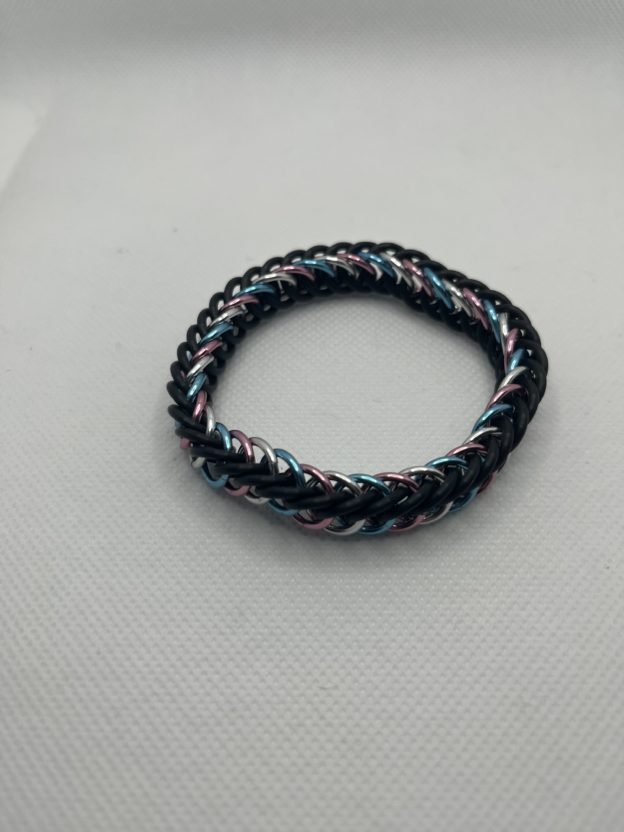 A chainmaille bracelet made with the persian 4 in 1 weave. This bracelet represents the Transgender Pride flag. It is made of black EPDM rings, and pink, lightblue, and silver anodized aluminium rings.