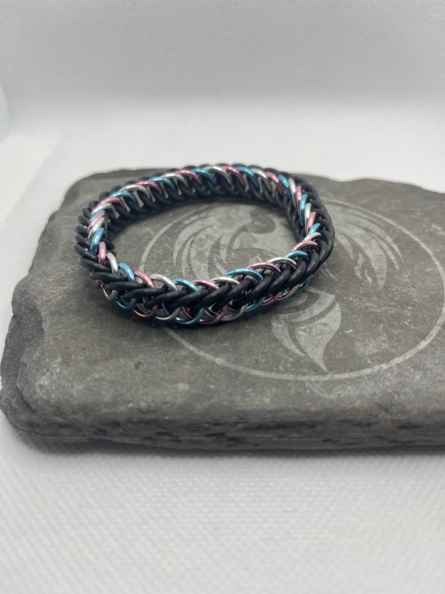 A chainmaille bracelet made with the persian 4 in 1 weave. This bracelet represents the Transgender Pride flag. It is made of black EPDM rings, and pink, lightblue, and silver anodized aluminium rings.