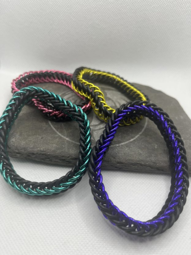 Four chainmaille bracelets created in the Persian 4 in 1 weave made with both anodized aluminum rings and EPDM rubber rings. All of the EPDM rings are black. The four bracelets are in colors of yellow, pink, sea green, and purple.