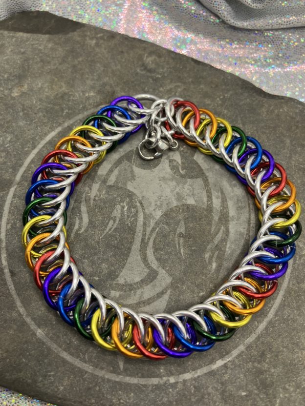 A chainmaille bracelet completed in the Persian 4 in 1 weave. It has alternating rings in the colors of the traditional pride flag--red, orange, yellow, green, blue, and purple. Silver rings are intermixed forming a bright backdrop to the alternating rings.