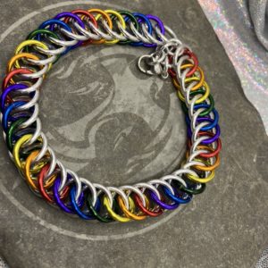 A chainmaille bracelet completed in the Persian 4 in 1 weave. It has alternating rings in the colors of the traditional pride flag--red, orange, yellow, green, blue, and purple. Silver rings are intermixed forming a bright backdrop to the alternating rings.