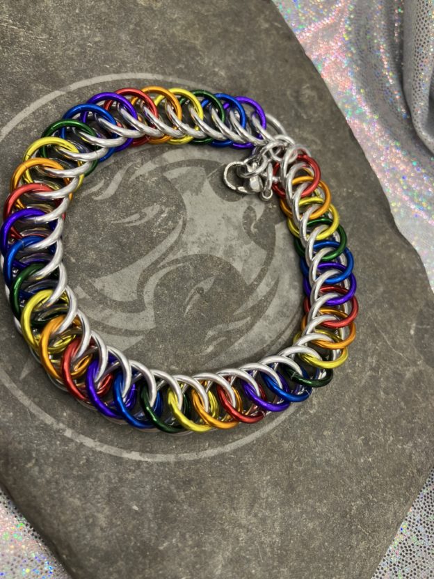 A chainmaille bracelet completed in the Persian 4 in 1 weave. It has alternating rings in the colors of the traditional pride flag--red, orange, yellow, green, blue, and purple. Silver rings are intermixed forming a bright backdrop to the alternating rings.