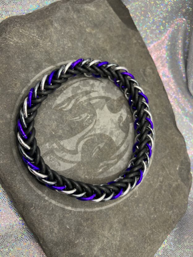 A chainmaille bracelet made with the persian 4 in 1 weave. This bracelet represents the Asexual Pride flag. It is made of black EPDM rings, and silver, gunmetal gray, and purple anodized aluminium rings.