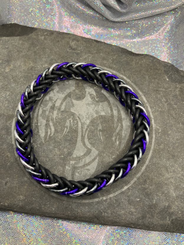 A chainmaille bracelet made with the persian 4 in 1 weave. This bracelet represents the Asexual Pride flag. It is made of black EPDM rings, and silver, gunmetal gray, and purple anodized aluminium rings.